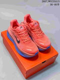 Pair of coral Nike Vomero Premium running shoes with blue soles on an orange shoebox.