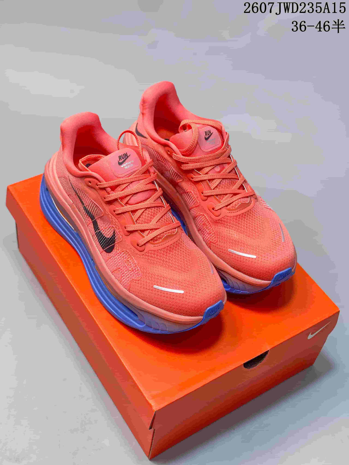 Pair of coral Nike Vomero Premium running shoes with blue soles on an orange shoebox.