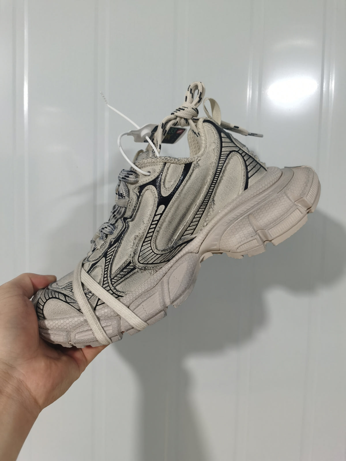 Side view of the beige and black sneakers showing layered textile panels, contrast detailing, laces, and the segmented outsole.