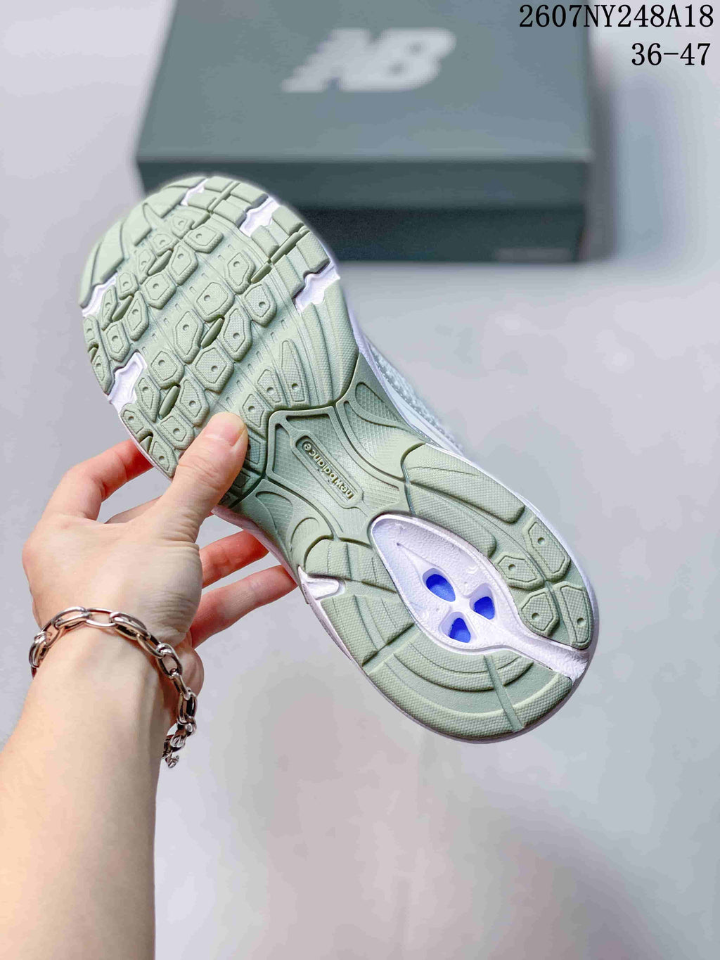 Underside view of a New Balance sneaker showing the patterned green-toned outsole and central support section.