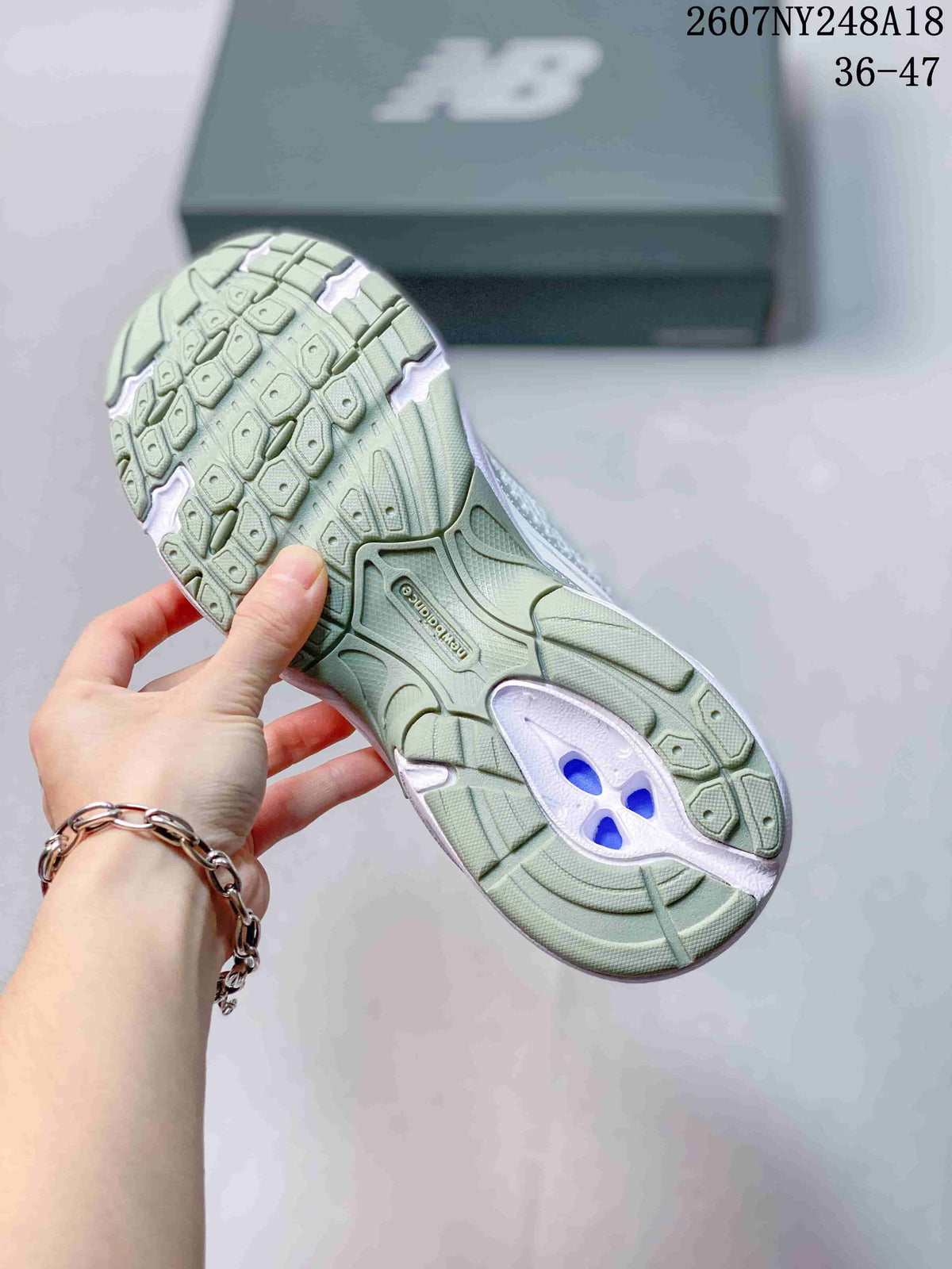 Underside view of a New Balance sneaker showing the patterned green-toned outsole and central support section.