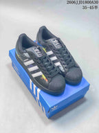 Pair of black Adidas Originals Superstar sneakers with white stripes, colorful splatter graphics, and textured shell toes on a blue box.