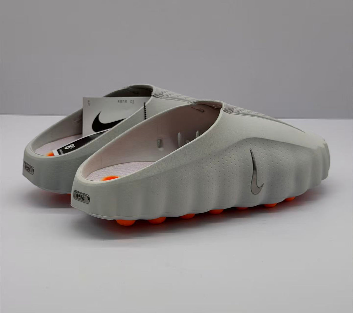 Rear three-quarter view of the gray slide sandals showing the open heels, side branding, and orange outsole elements.