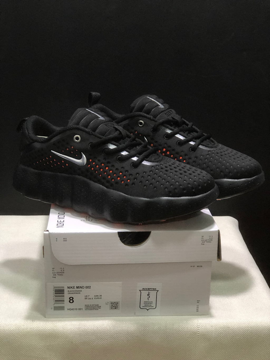 Three-quarter product view of the pair on the shoebox, with the Nike Mind 002 label and style code visible.