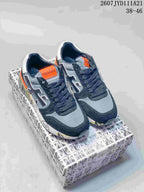 Pair of grey and navy Premiata sneakers with orange accents displayed on a patterned shoebox.