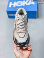 Top view of a light-colored HOKA running shoe showing the lace-up closure, padded tongue, dark toe overlay, and orange side accent.