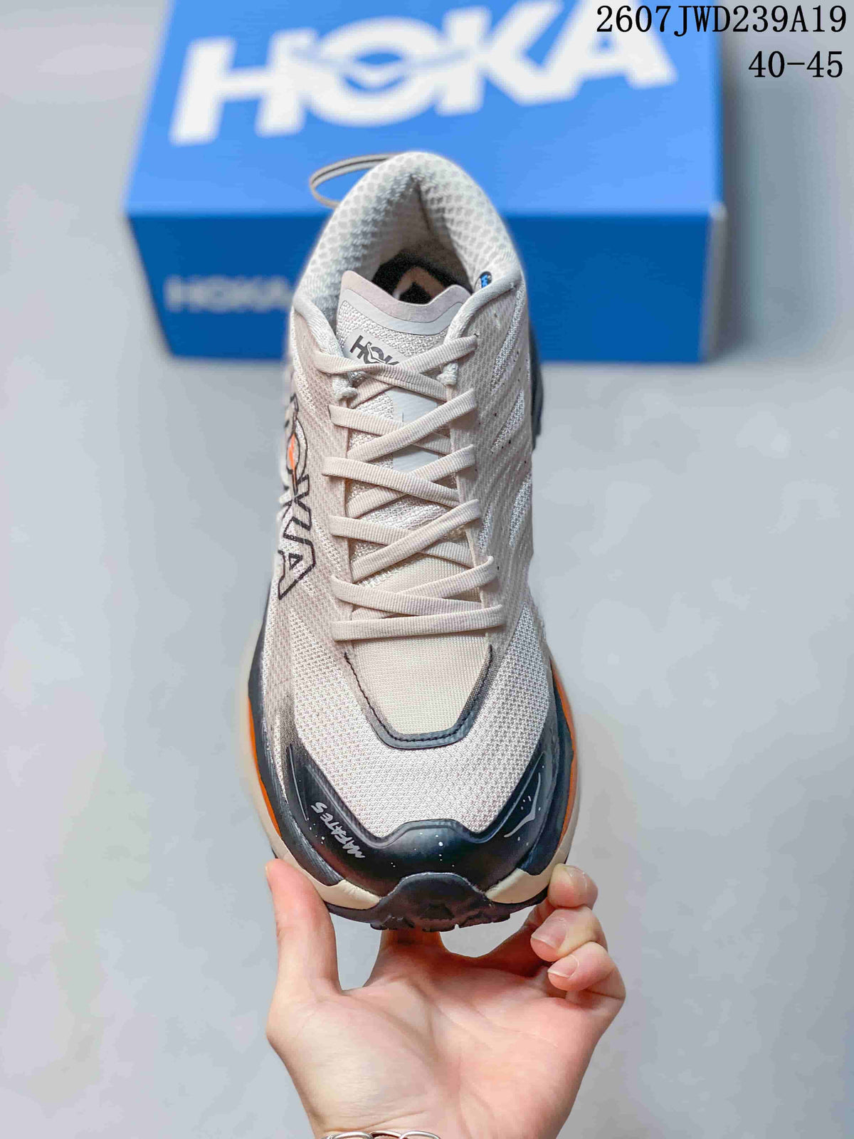 Top view of a light-colored HOKA running shoe showing the lace-up closure, padded tongue, dark toe overlay, and orange side accent.