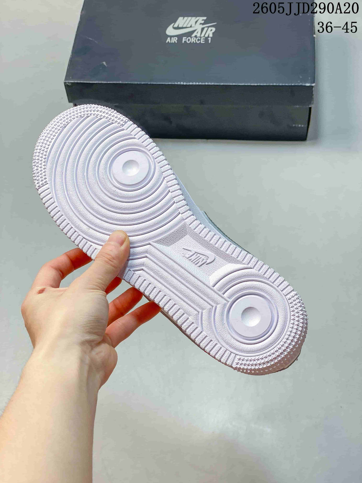 Bottom view of the white sneaker outsole showing circular traction patterns and textured rubber detailing; shoebox in the background displays Nike Air Force 1 branding.