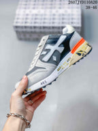 Side view of a grey, navy and white Premiata sneaker with layered panels, orange heel detail and printed midsole; image text shows 2607 TYD110A20 and 38–46.