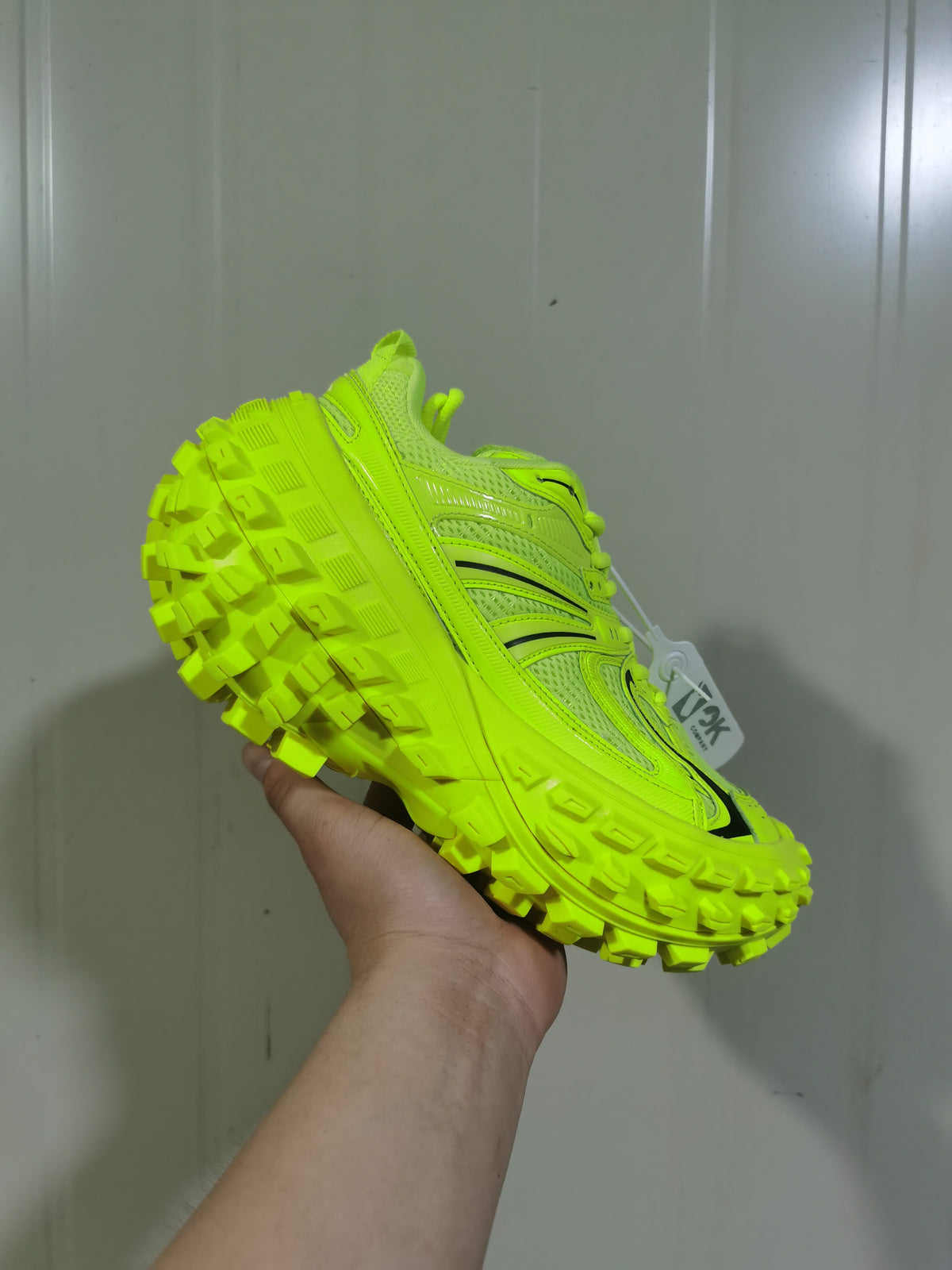 Angled rear-side view of the bright green sneaker, highlighting the raised heel, layered upper, and heavily lugged rubber outsole.
