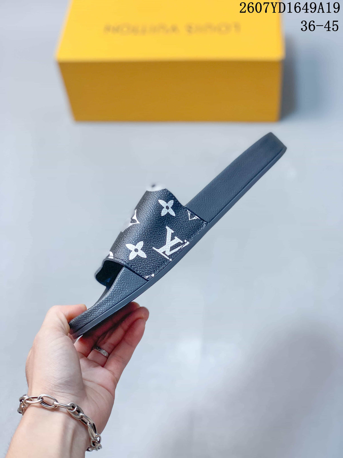 Side profile showing the wide patterned strap and raised sole of the black slide sandal.