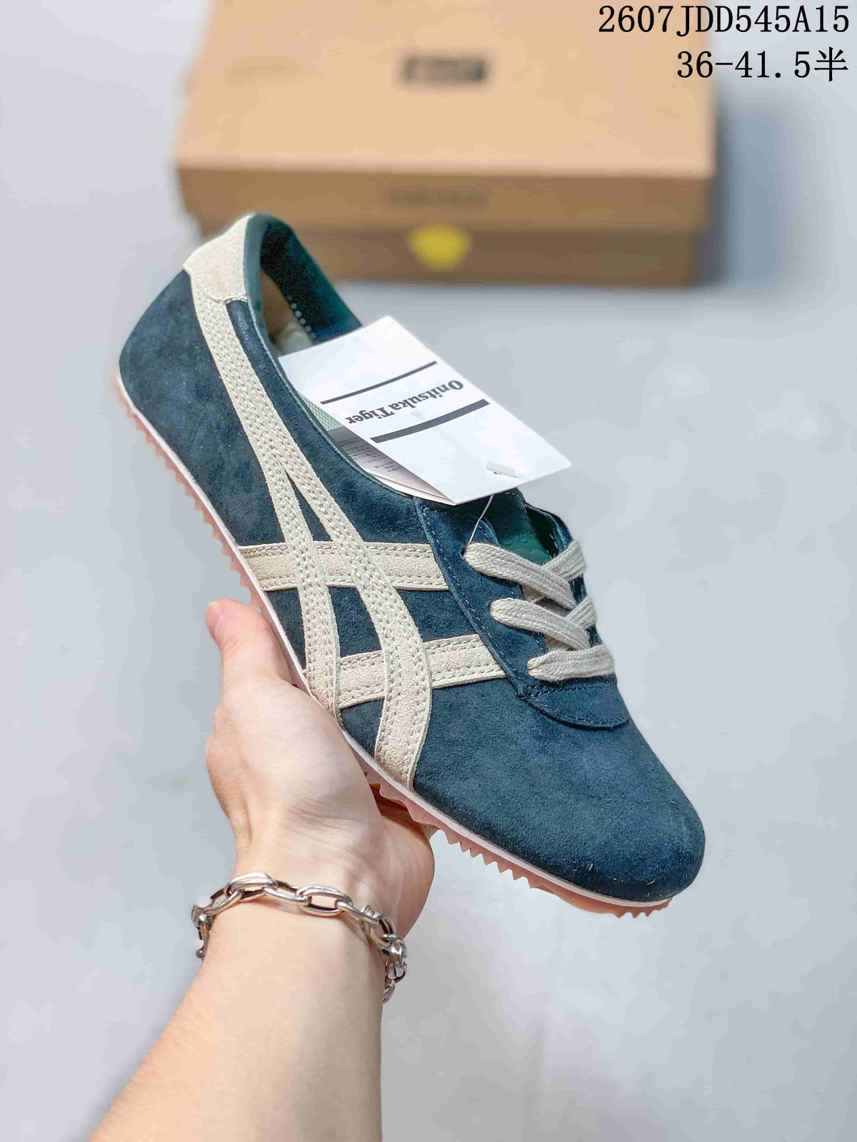 Navy suede-style low-top sneaker with light side stripes, gray laces, and a tan textured outsole, shown with a shoe box.