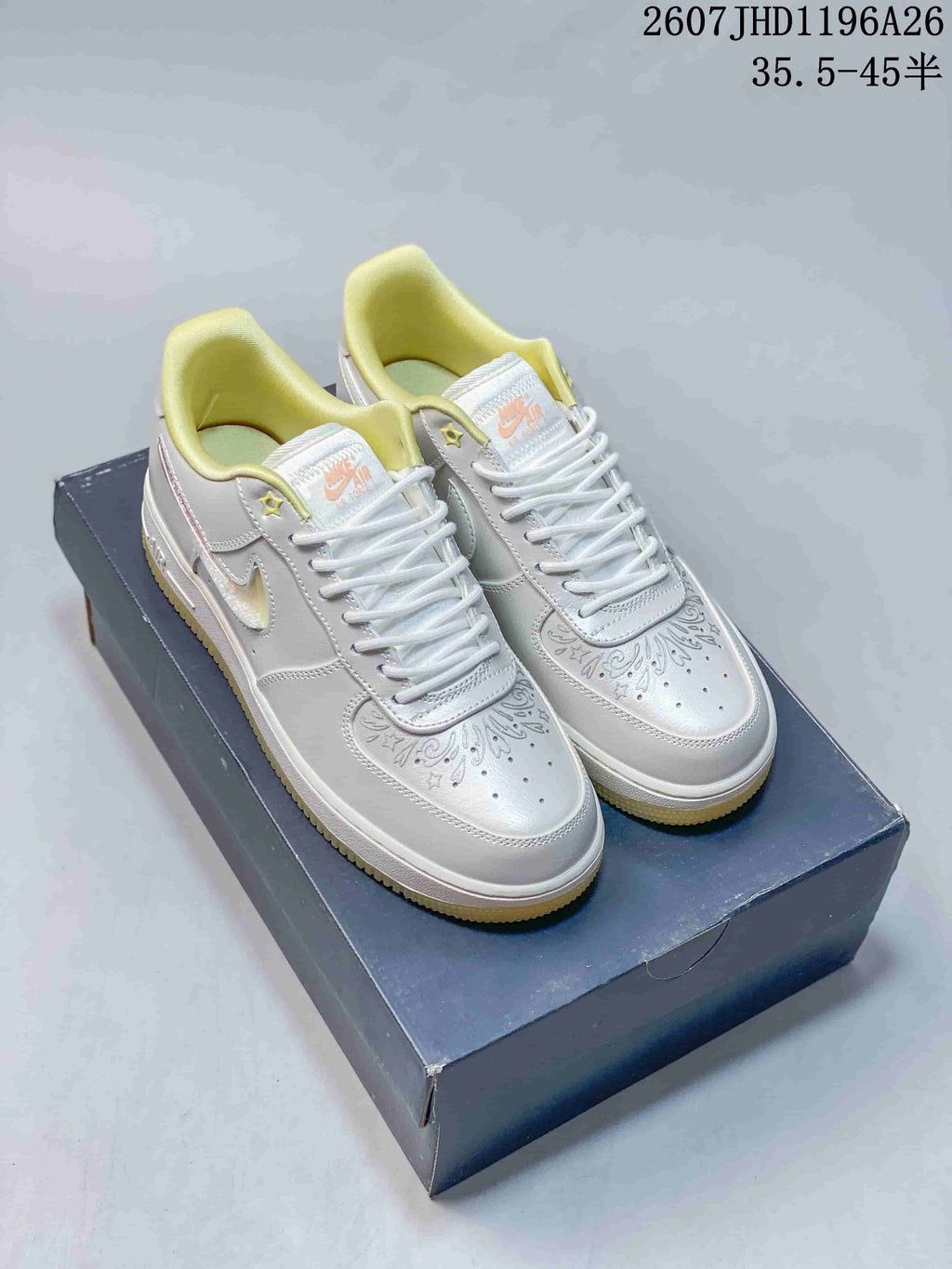 Pair of white and yellow Nike Air Force 1 ’07 LV8 low-top sneakers displayed on a shoebox, showing the decorated toe boxes and yellow collar lining.