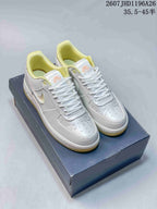 Pair of white and yellow Nike Air Force 1 ’07 LV8 low-top sneakers displayed on a shoebox, showing the decorated toe boxes and yellow collar lining.