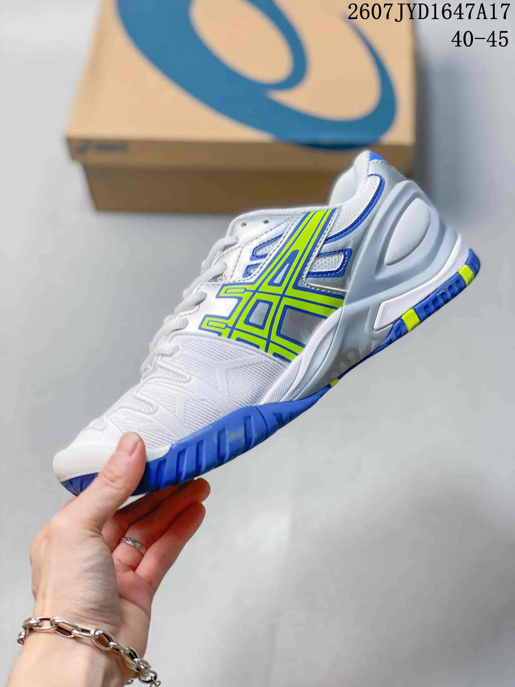 Side view of the white ASICS tennis shoe showing blue and neon yellow side branding, a structured heel area and blue outsole.