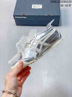 Side view of a silver low-top sneaker with cream stripes, sheer bow laces, and textured outsole.