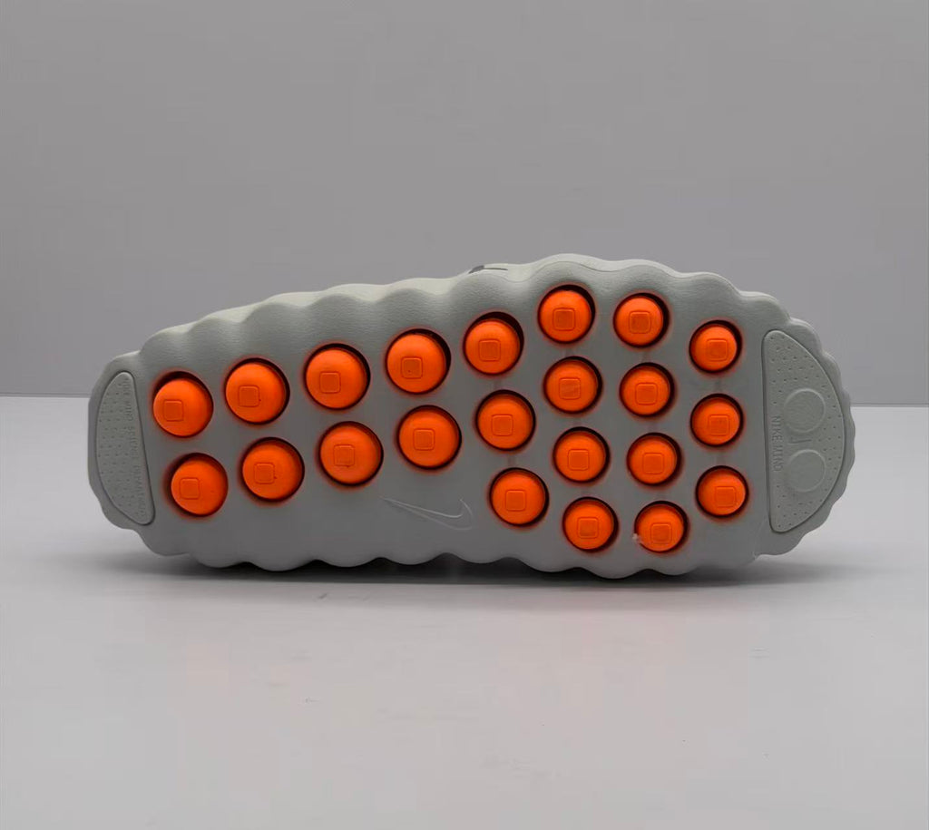 Outsole view of the gray slide sandal showing multiple orange circular elements and molded tread details.