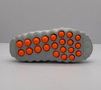 Outsole view of the gray slide sandal showing multiple orange circular elements and molded tread details.