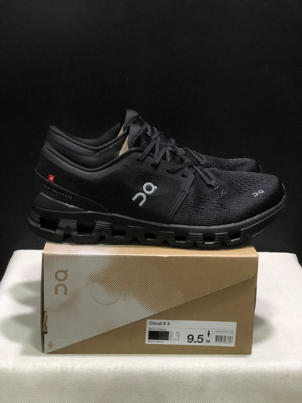 Side view of black On Cloud X4 shoes showing the branded upper, heel detail and segmented outsole.