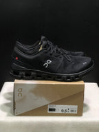 Side view of black On Cloud X4 shoes showing the branded upper, heel detail and segmented outsole.