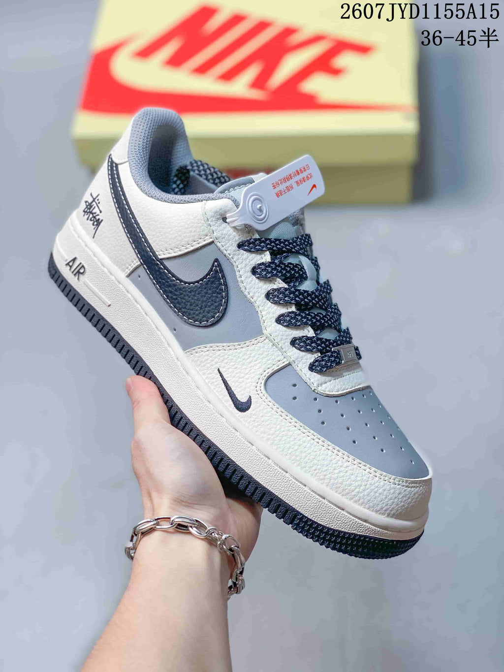 Angled side view of the grey and white Nike Air Force 1 sneaker with navy Swoosh, navy laces, AIR midsole branding and dark outsole.