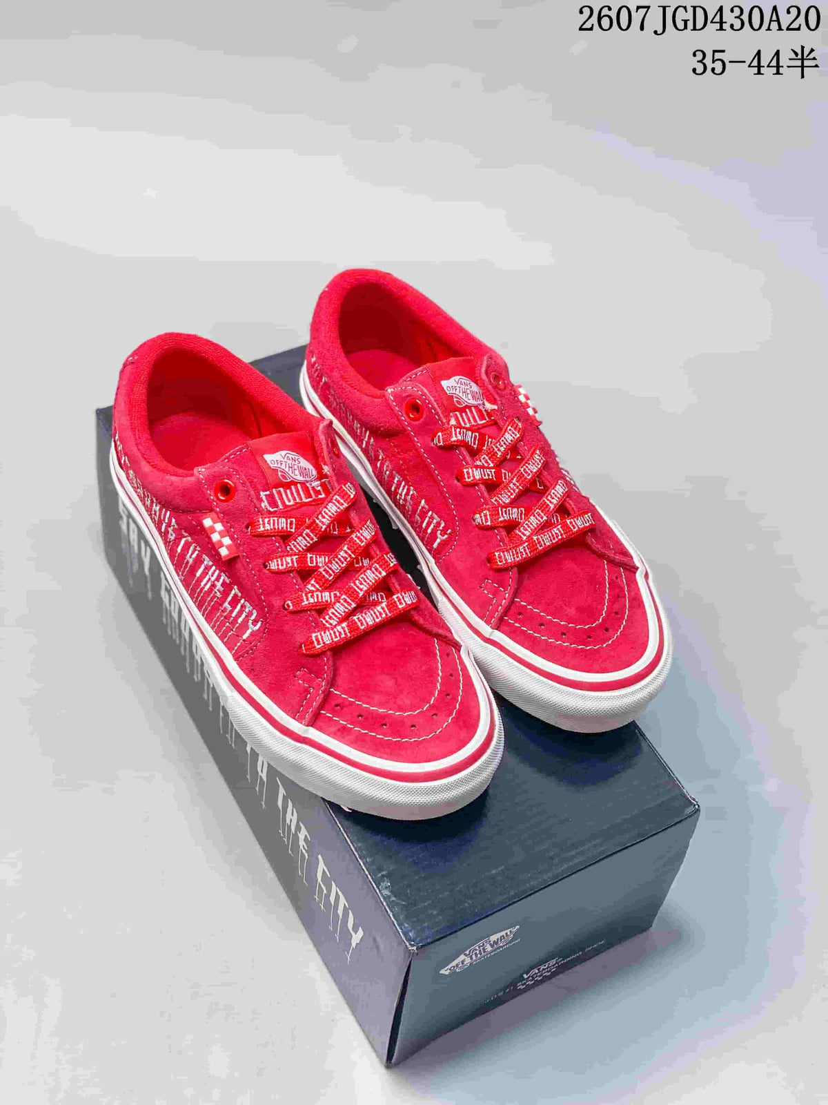 Pair of red Vans low-top sneakers displayed on a branded shoebox, showing patterned laces, white side stripes, and contrast stitching.