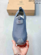 Top view of the sneaker showing the blue-gray mesh upper, front pull tab, branding patch, and protective toe panel.