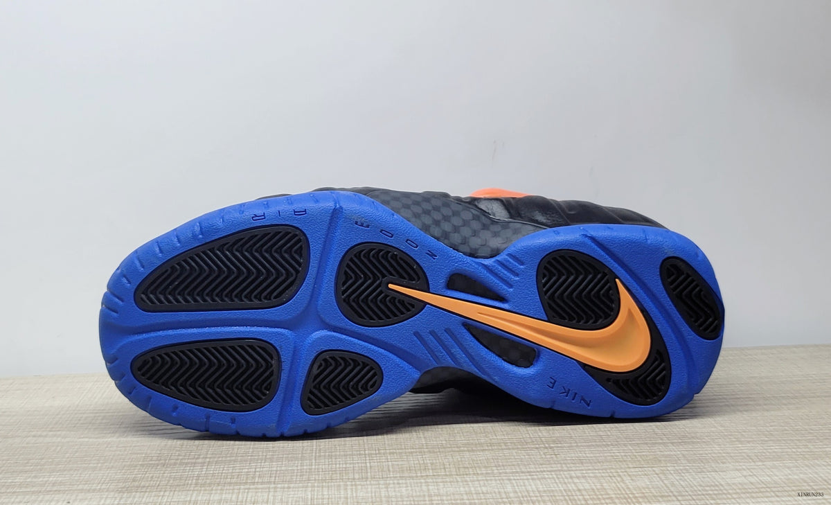 Underside of black Nike Air Foamposite Pro sneakers showing a bright blue outsole and orange Swoosh.