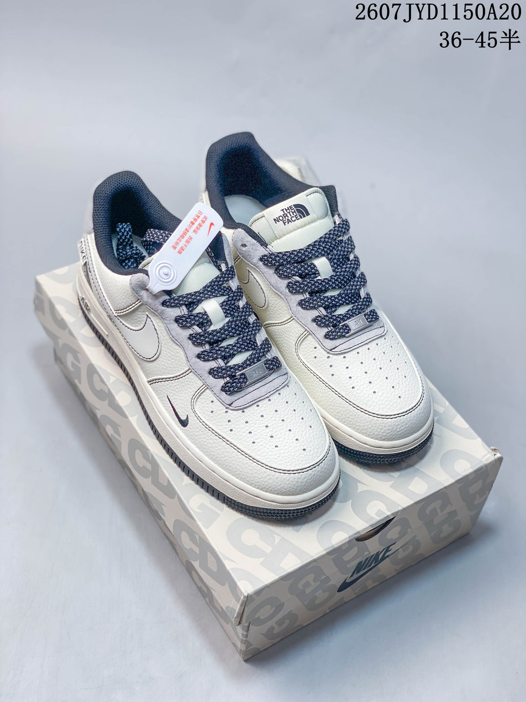 Pair of white Nike Air Force 1 '07 low-top sneakers with navy laces and gray details displayed on a patterned shoebox.
