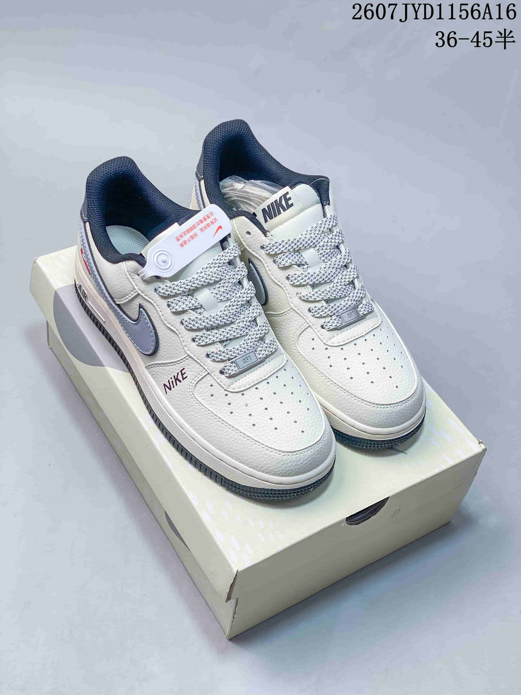 White low-top sneakers with grey accents and patterned side details displayed on a light-colored shoe box.