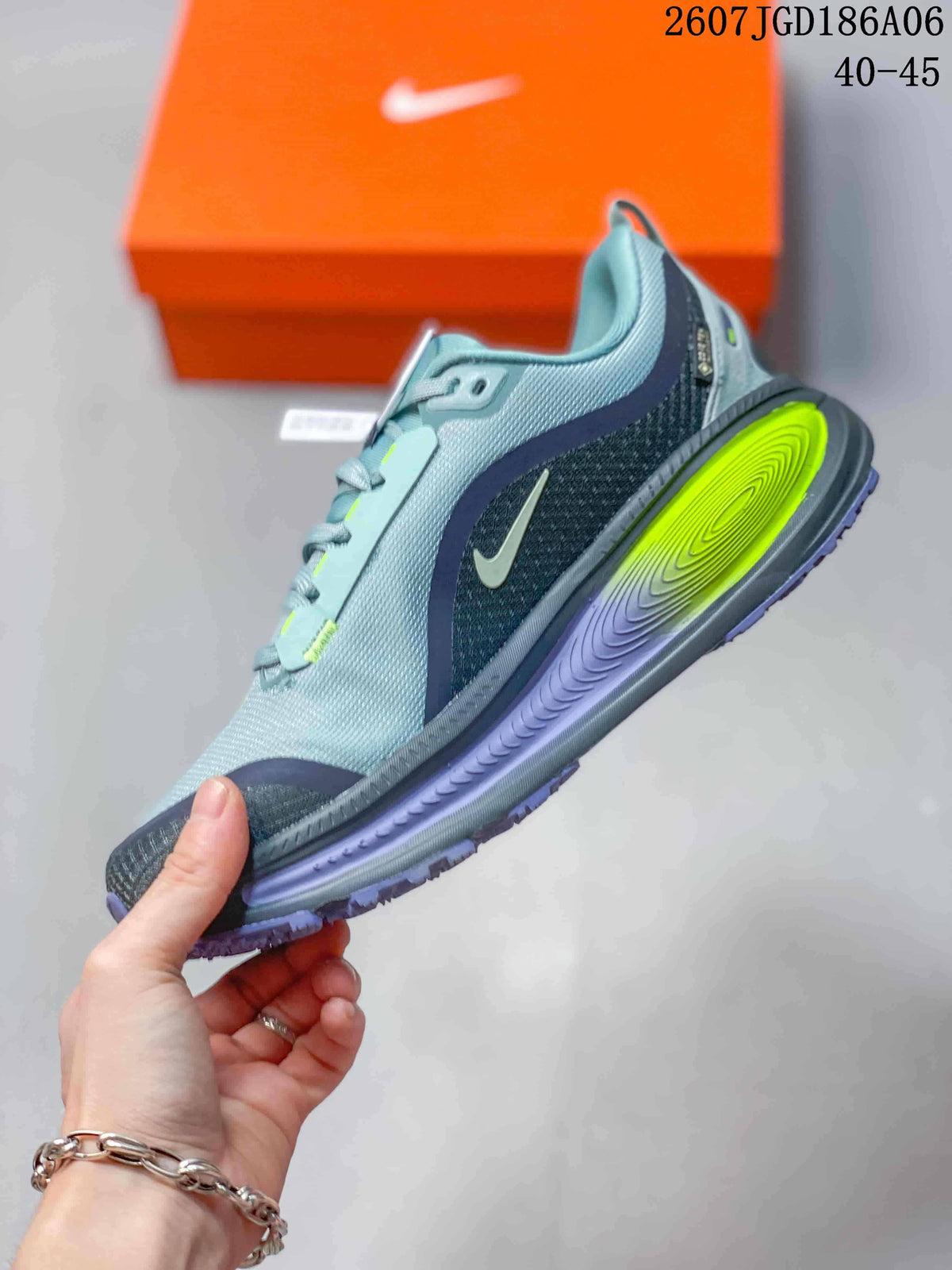 Side profile of the gray sneaker showing the layered textile-style upper, Nike Swoosh, neon yellow midsole insert, and purple outsole.