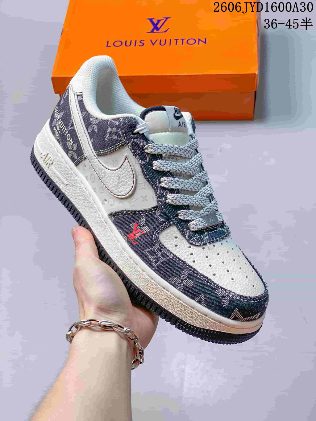 Cream and dark monogram-print low-top sneaker with a contrast swoosh, held in front of an orange box.