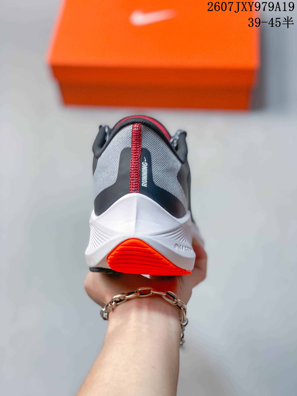 Rear view of the Nike running shoe showing the padded heel, gray upper, white midsole, and orange outsole section; image text shows style code 2607JXY979A19 and size range 39–45.