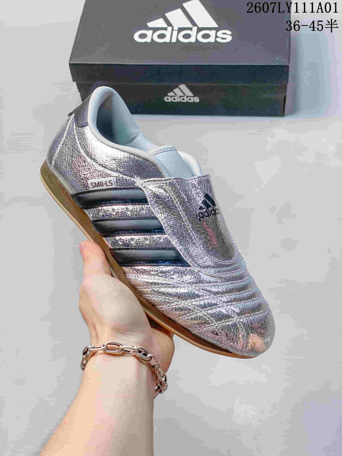 Metallic silver Adidas Taekwondo low-top slip-on sneaker with dark stripes and a gum-colored outsole.
