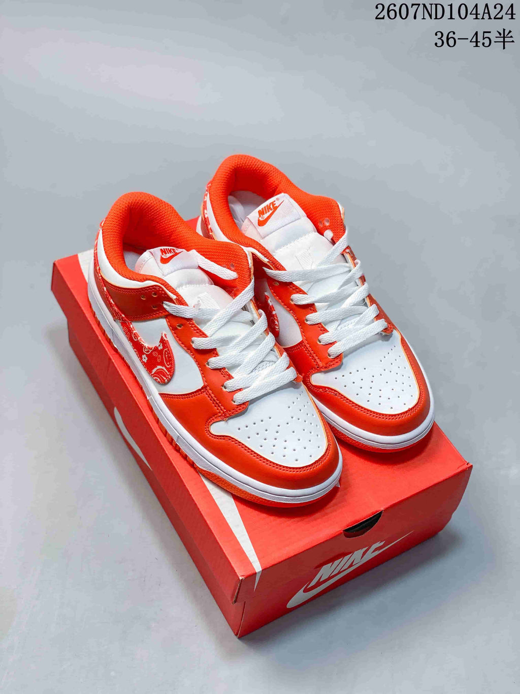 White and orange Nike SB Dunk Low sneakers displayed on a red shoebox.