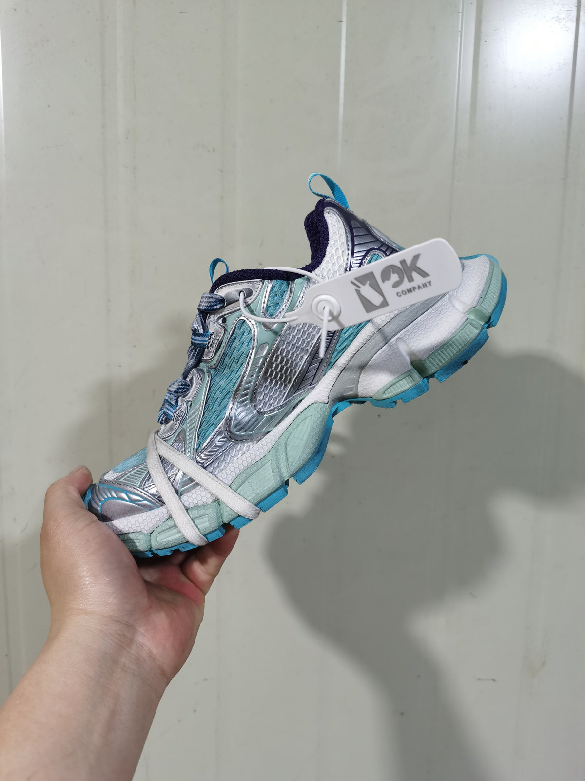 Side view of a light blue, white, silver and purple sneaker showing layered mesh panels, laces, padded collar and blue outsole accents.