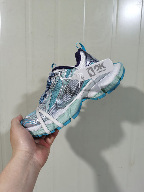 Side view of a light blue, white, silver and purple sneaker showing layered mesh panels, laces, padded collar and blue outsole accents.