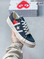 Close-up of a navy low-top sneaker showing the side stripes, star emblem, heart-eye graphic and white rubber outsole.