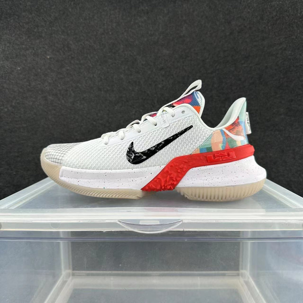 Side view of a white Nike basketball shoe with a black Swoosh, red midsole accents, and multicolor heel details.