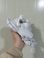 Angled view of a white Nike sneaker showing the laces, layered panels, mesh details, and segmented sole.