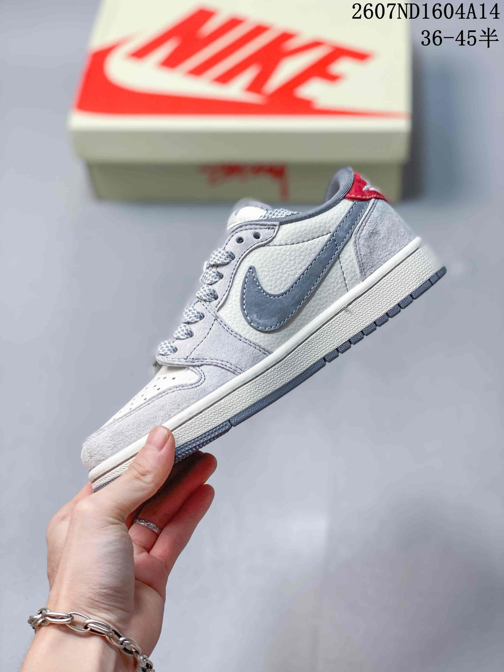Side view highlighting the gray side overlays, off-white upper, red accent, white midsole, and textured outsole.