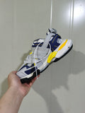 Balenciaga Track sneaker held at an angle, showing white, navy blue and yellow layered panels with a black outsole.