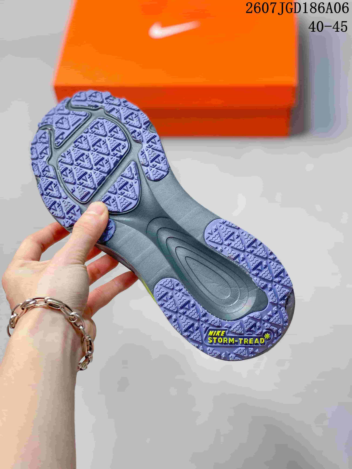 Underside view of a sneaker showing a patterned purple outsole and a visible Nike Storm-Tread marking, with an orange shoebox in the background.