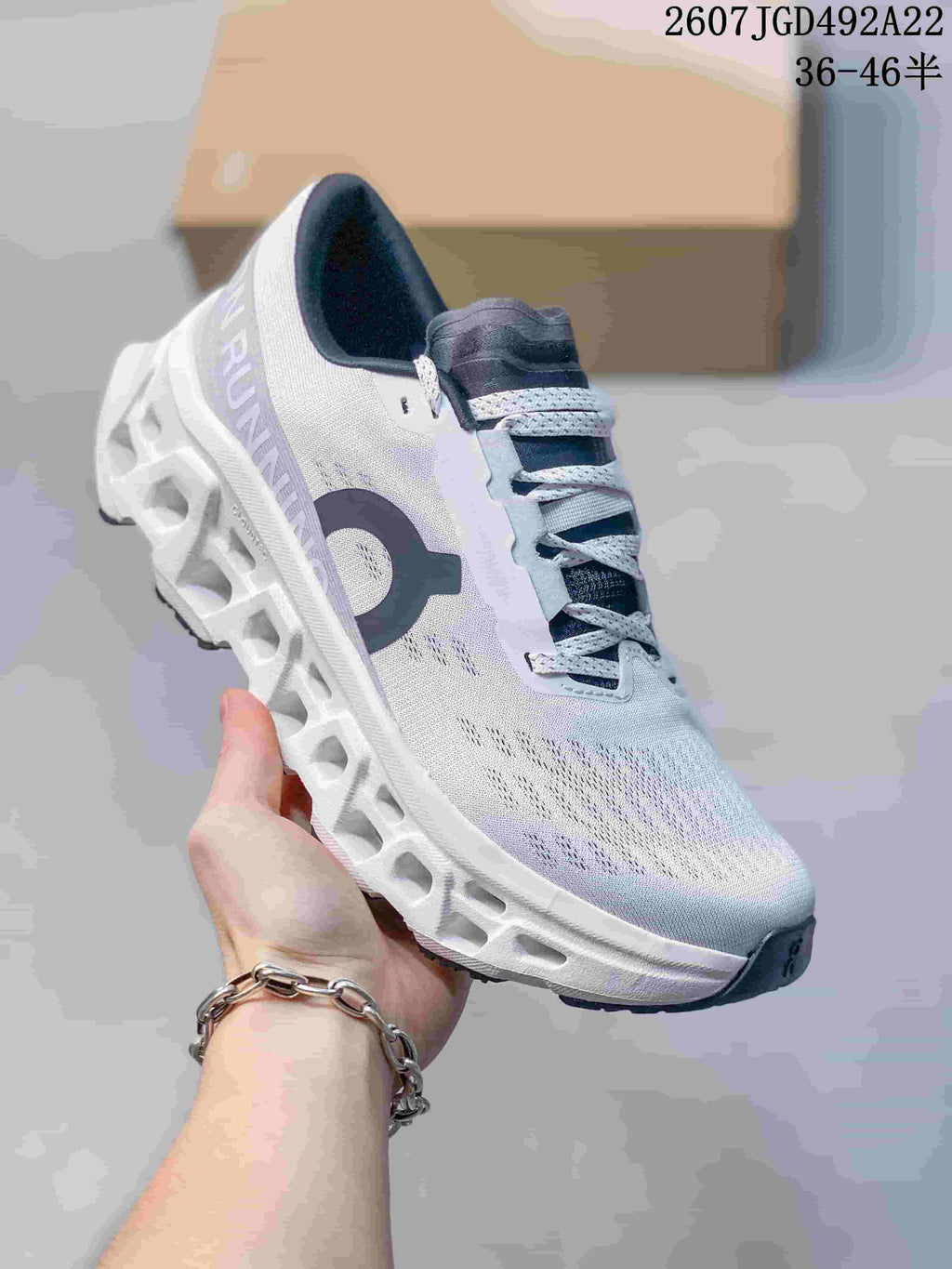 Angled side view of the white and gray On running shoe showing the side branding, lace-up construction, and sculpted outsole; the image displays style code 2607JGD492A22 and size range 36–46.