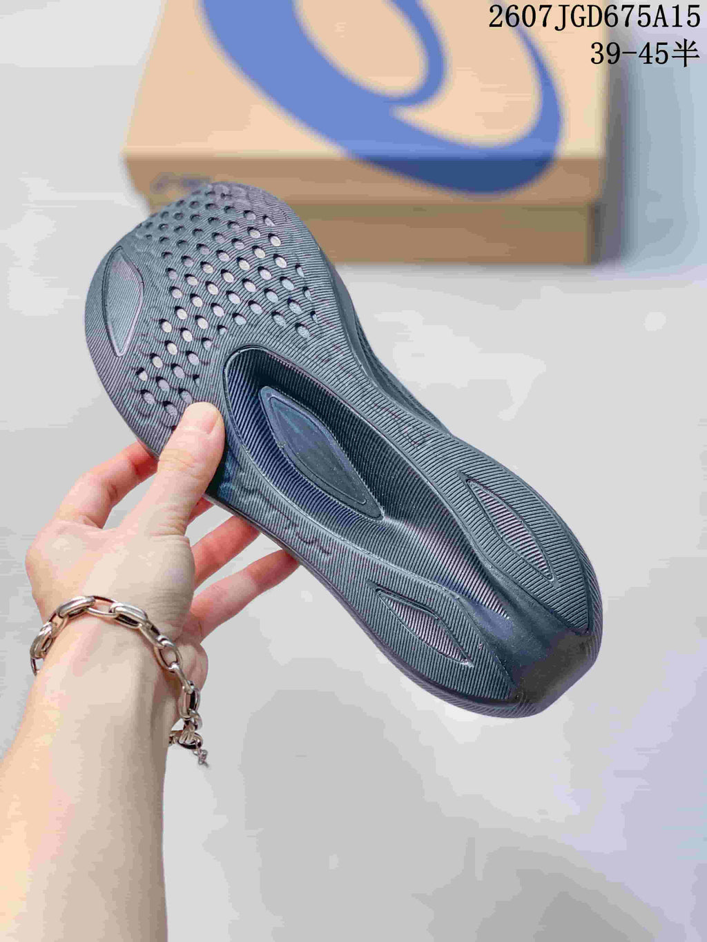 Close-up of the patterned outsole on a dark gray ASICS running shoe; overlay text shows product code 2607TGD675A15 and a 39–45 half-size range.