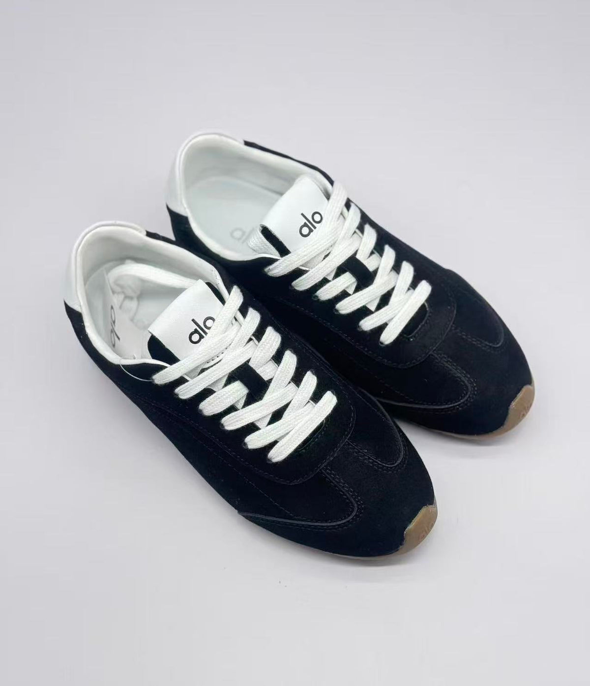 Top three-quarter view showing the pair's black uppers, white laces, and Alo tongue branding.