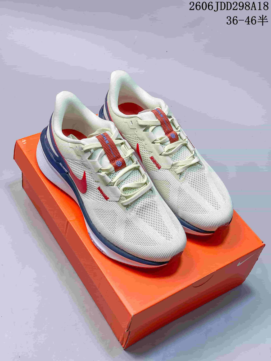 Pair of white Nike running sneakers with red and blue accents displayed on an orange shoebox.