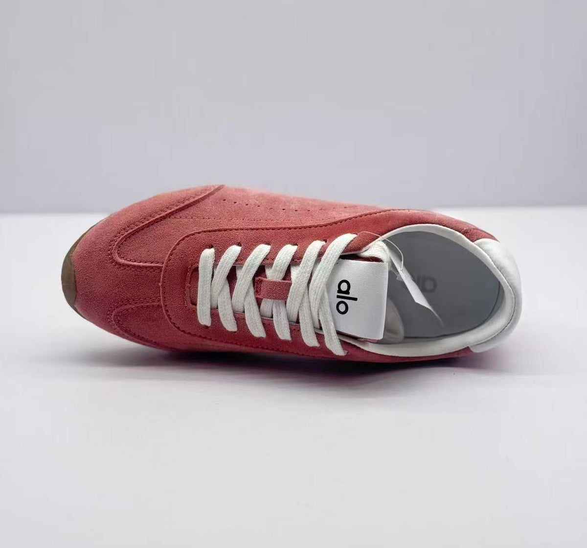 Top view of one pink sneaker showing the white laces, tongue label and padded collar.