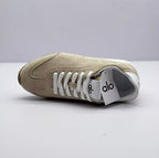 Side and top view of one beige sneaker with white laces and visible tongue branding.