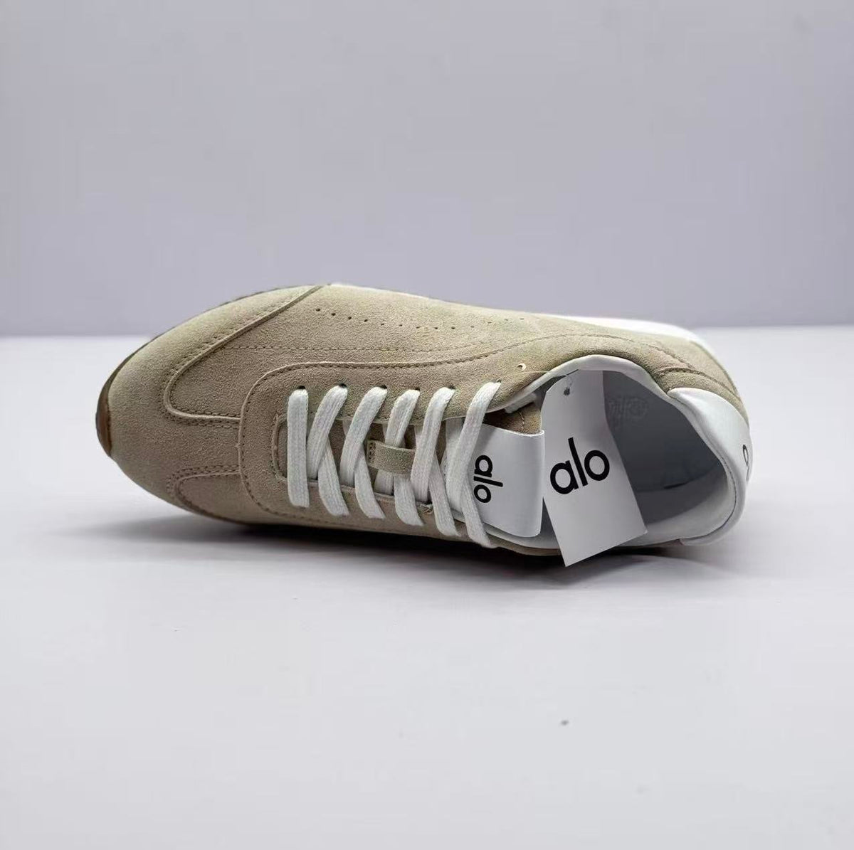Side and top view of one beige sneaker with white laces and visible tongue branding.